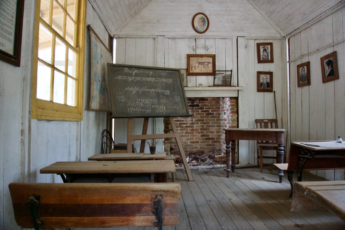 picture of 1800s classroom with blackboard, seats and a teacher's desk.